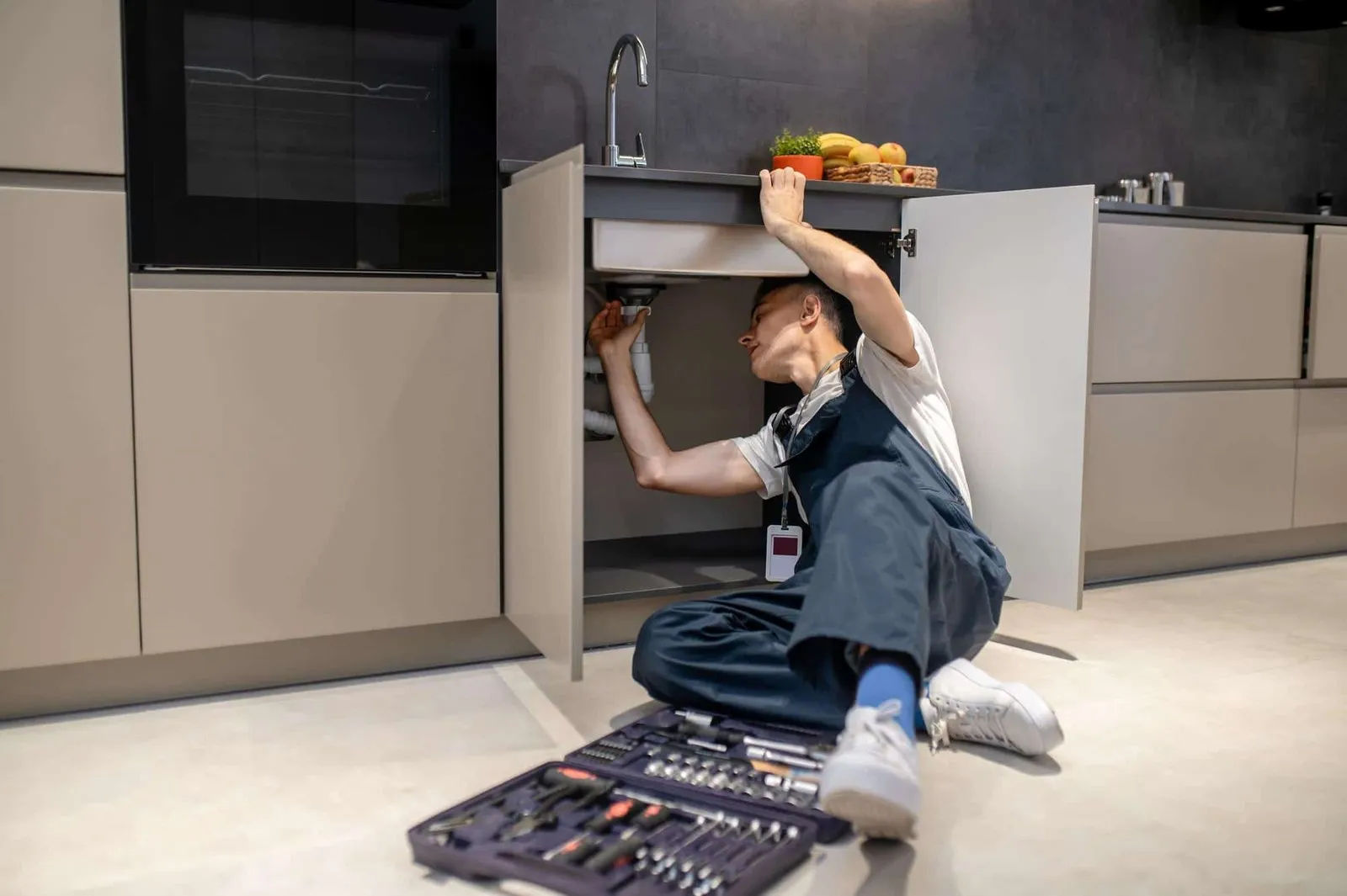 Technicien réalisant un diagnostic de fuite sous un évier.